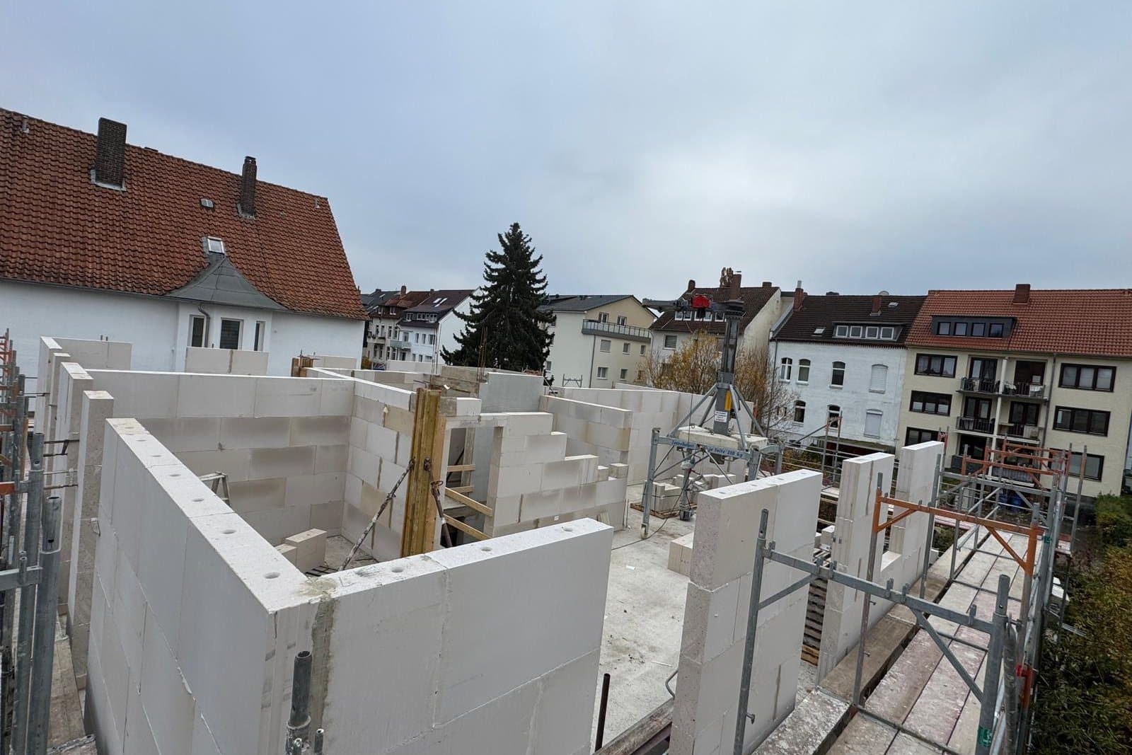 Rohbau aus großformatigen Kalksandsteinen: frisch gemauerte Innen- und Außenwände eines Obergeschosses, ringsum Gerüst und Nachbarhäuser