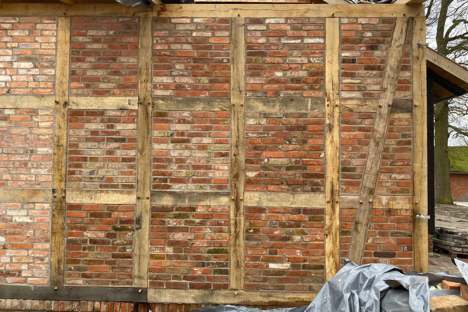 Fachwerkwand bei der Sanierung: alte Holzbalken mit neu ausgemauerten Gefachen aus rotem Ziegel