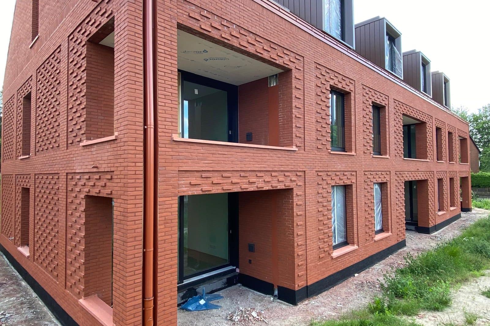 Neubau mit roter Klinkerfassade und Ziermauerwerk aus vor- und zurückspringenden Steinen an Loggien und Fensterfeldern
